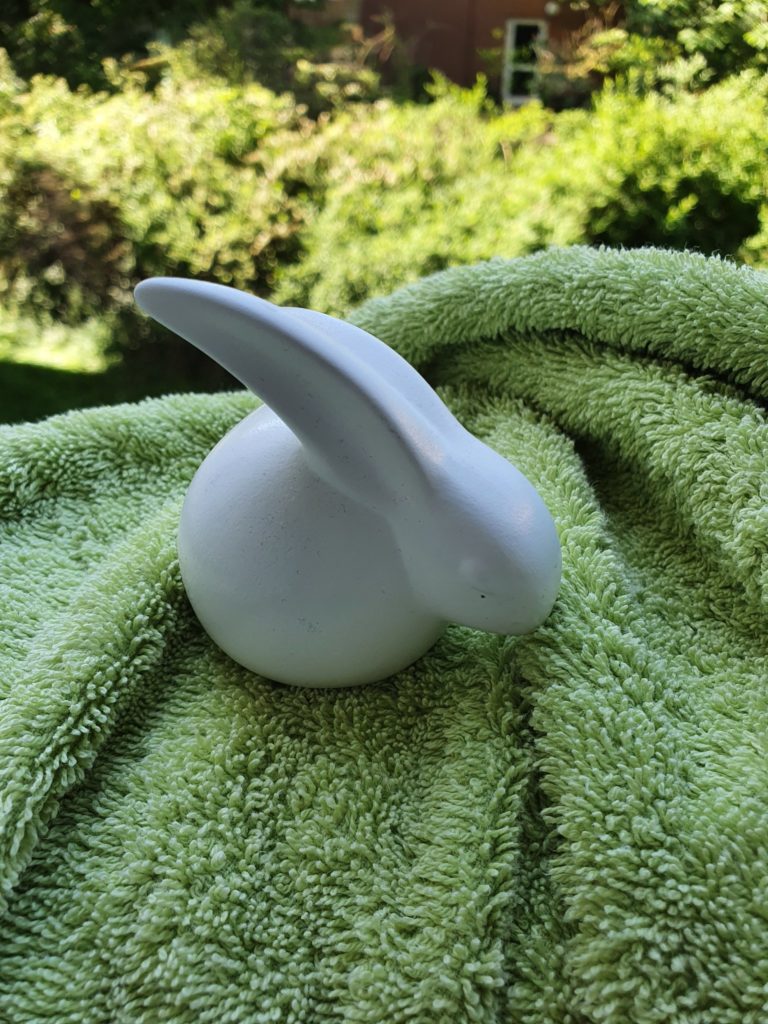 Stilisierte Hasen-Ton-Figur, weiß, vor grünem Hintergrund.